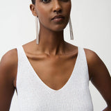 Woman wearing a white sleeveless top with long earrings on a plain background