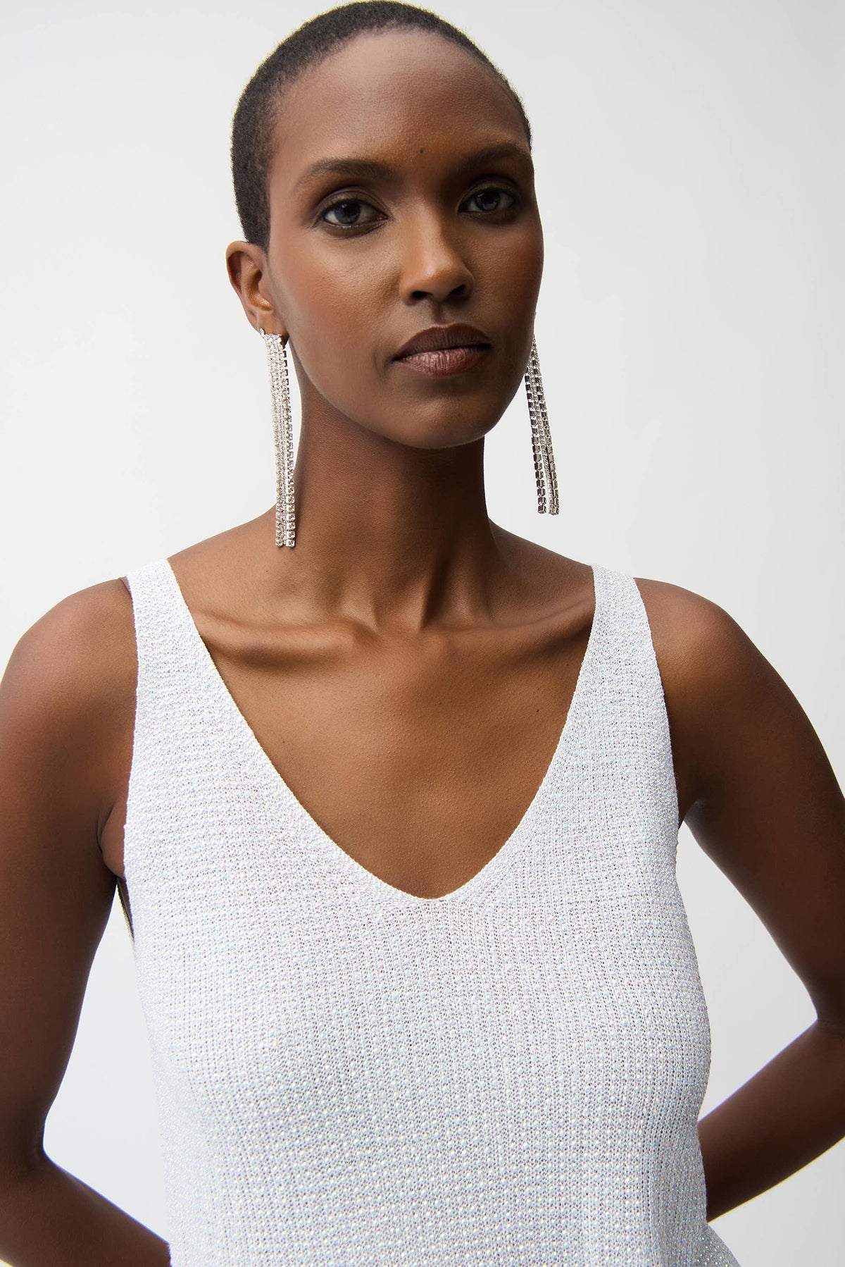 Woman wearing a white sleeveless top with long earrings on a plain background