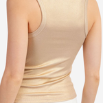 Model wearing gold tank top with white pants on a white background.