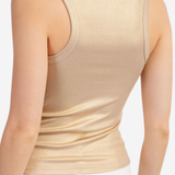 Model wearing gold tank top with white pants on a white background.