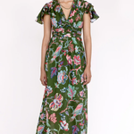 A model wearing a green midi dress with a colorful floral and bird print, featuring flutter sleeves and a tie-waist detail, set against a plain white studio background.