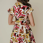 A woman shown from behind wearing a short-sleeve collared dress with a bold abstract floral pattern in red, brown, olive green, and cream on a light background.