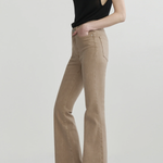 A model wearing beige flared jeans and a black sleeveless top, standing against a light gray studio background.