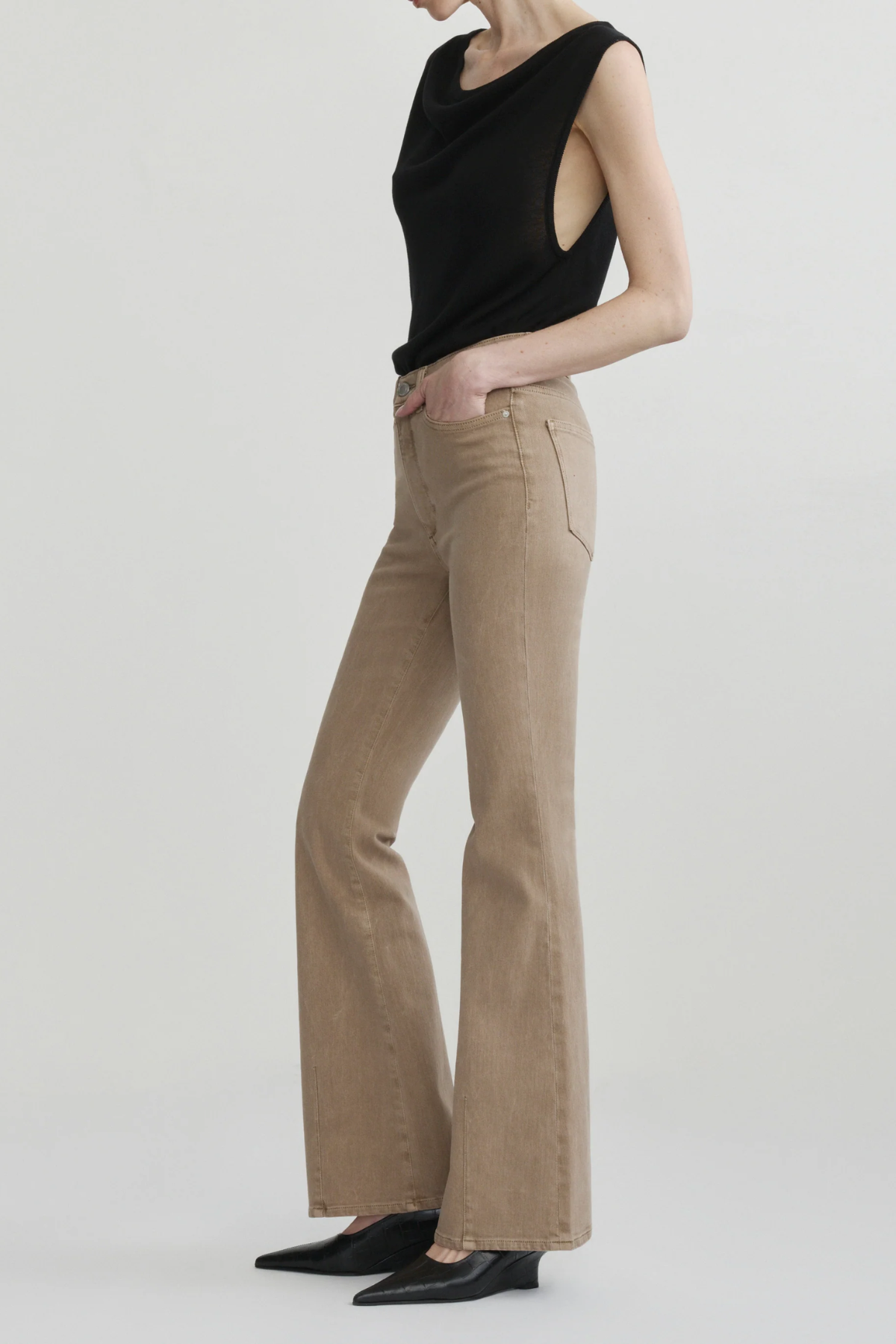 A model wearing beige flared jeans and a black sleeveless top, standing against a light gray studio background.