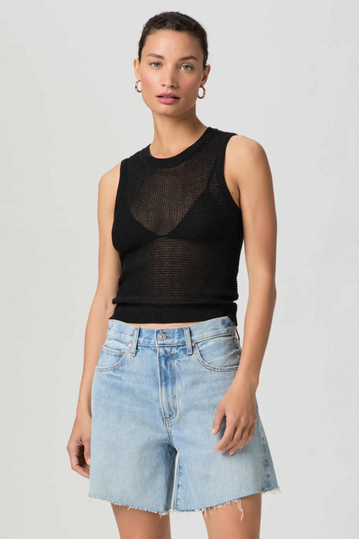 Woman wearing a black sleeveless top and light blue denim shorts on a gray background