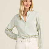 Woman wearing a light green blouse and white pants against a beige background