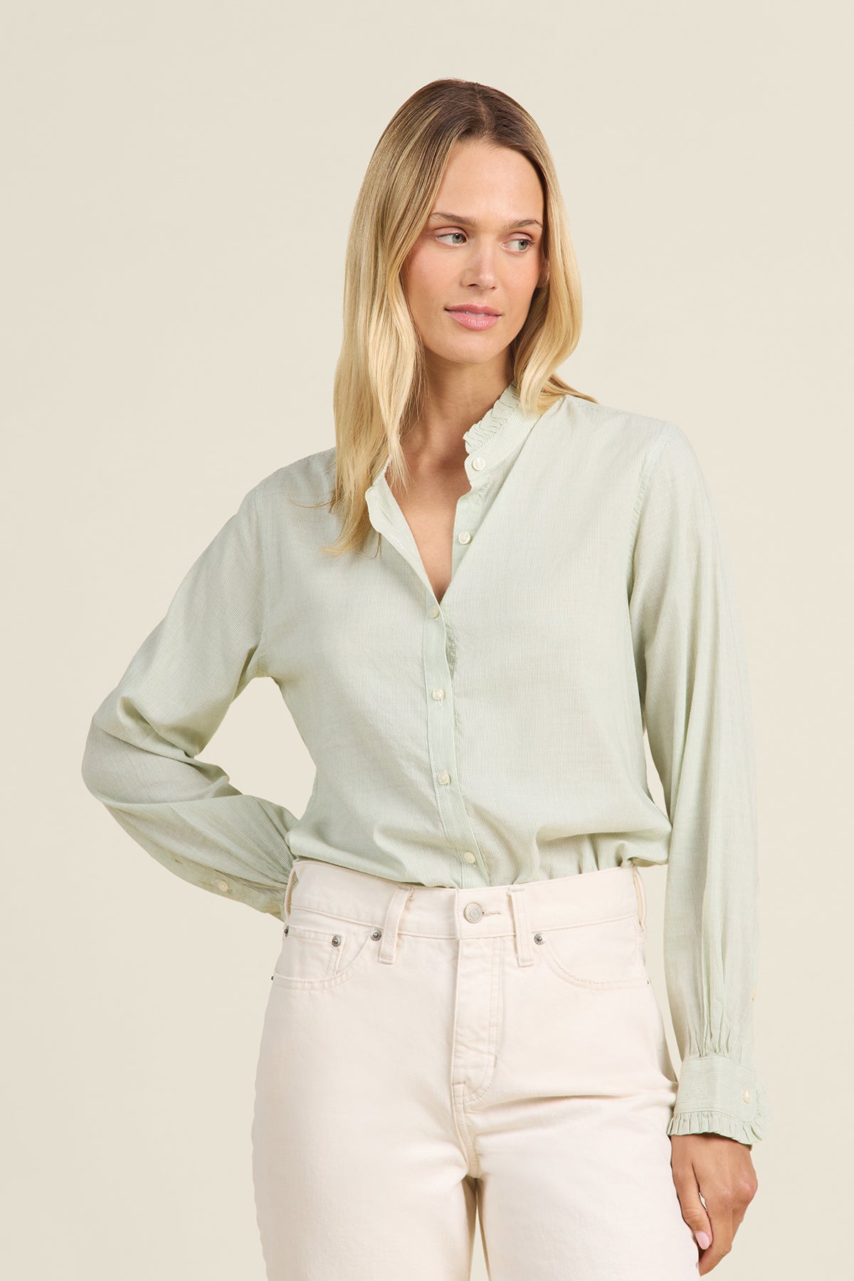 Woman wearing a light green blouse and white pants against a beige background
