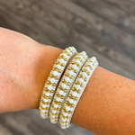Beaded bracelet with white beads and gold metal links, worn on a person's wrist against a blurred wood background.