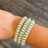 Beaded bracelet with white beads and gold metal links, worn on a person's wrist against a blurred wood background.