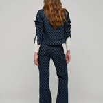 A model viewed from the back wearing a dark navy blue patterned jacket and matching flared pants over a cream long-sleeve shirt, set against a plain light gray studio background.