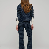 A model viewed from the back wearing a dark navy blue patterned jacket and matching flared pants over a cream long-sleeve shirt, set against a plain light gray studio background.