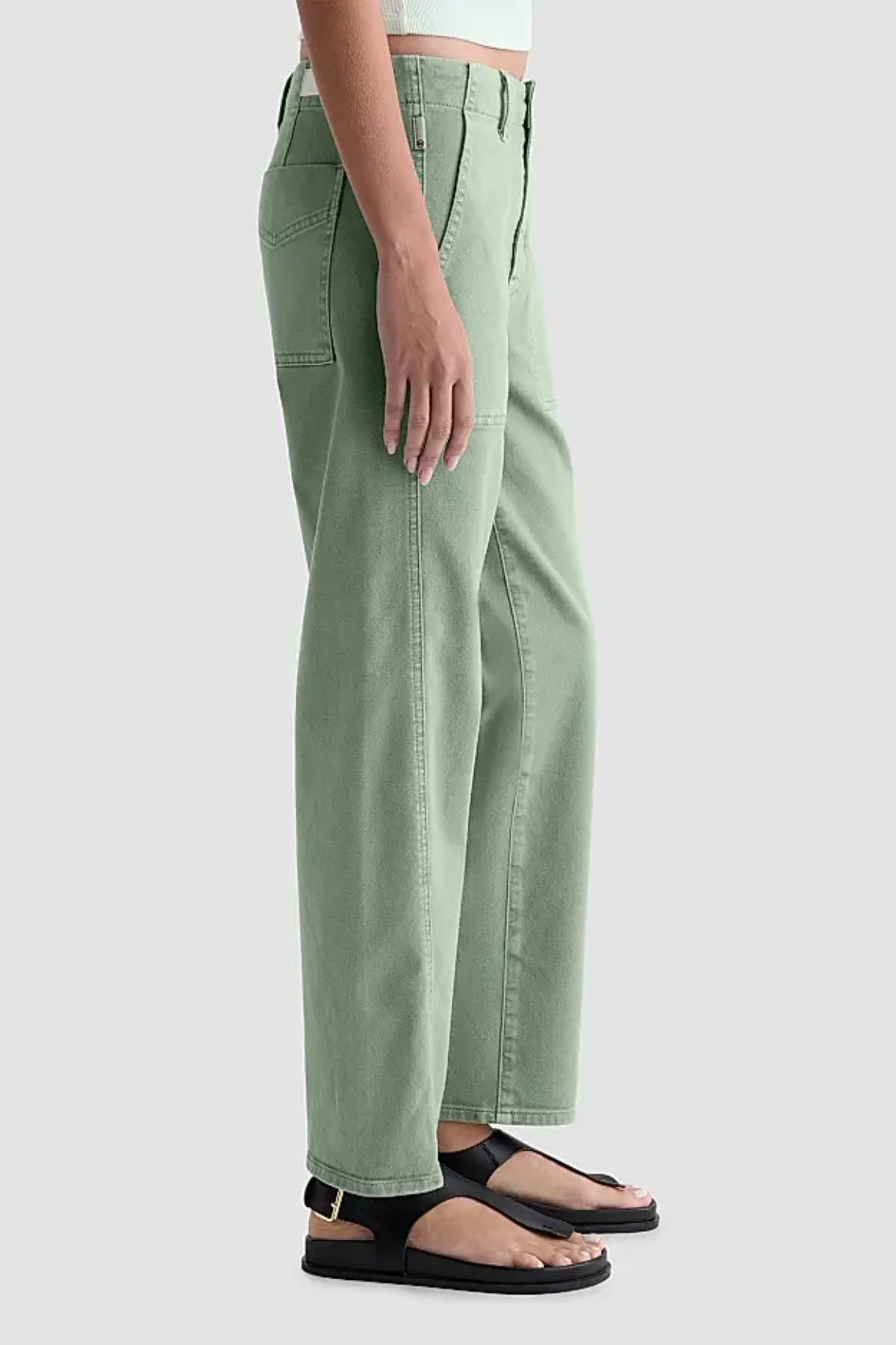 A person shown from the waist down wearing sage green wide-leg cropped pants with black flat sandals, against a light gray studio background.