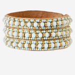 A wide leather cuff bracelet decorated with multiple rows of light blue and white beads accented by small gold beads, shown on a plain light gray background.