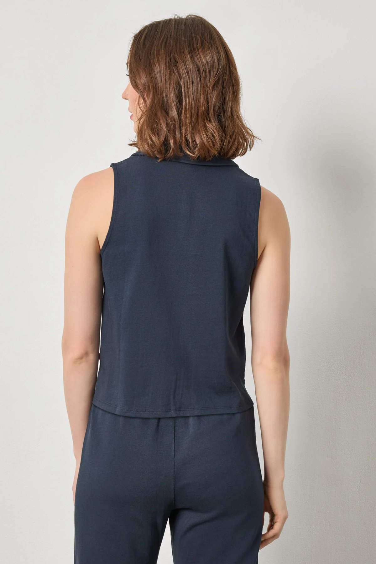 Person wearing a navy sleeveless top and pants on a light gray background