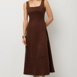 A woman modeling a sleeveless brown midi dress with a square neckline and a flared skirt, paired with snakeskin-patterned boots, against a plain light gray studio background.