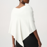 A model wearing a cream-colored wrap shawl with a fluffy pom-pom detail at the center, styled over a black top against a light gray studio background.