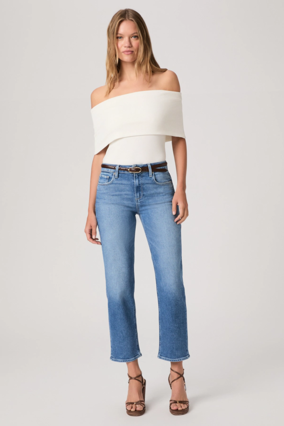Woman wearing a white off-shoulder top and blue jeans on a white background