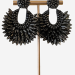 A pair of large black beaded dangle earrings displayed on a gold-tone jewelry stand against a light gray background.