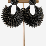 A pair of large black beaded dangle earrings displayed on a gold-tone jewelry stand against a light gray background.