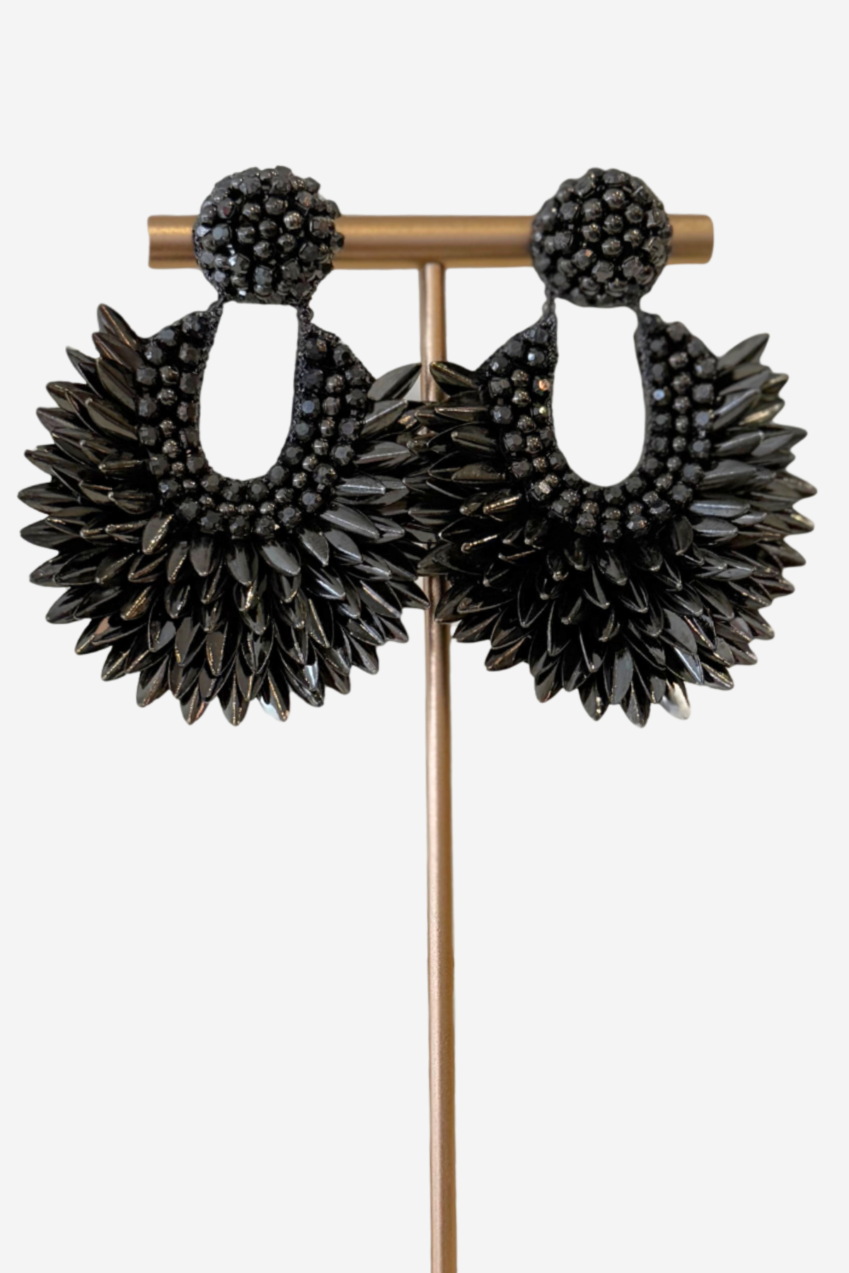 A pair of large black beaded dangle earrings displayed on a gold-tone jewelry stand against a light gray background.