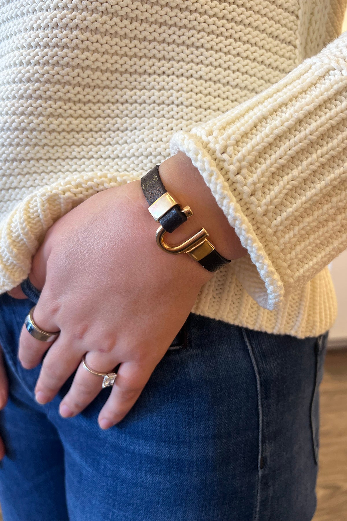 Hand wearing a gold bracelet with a beige sweater and blue jeans.
