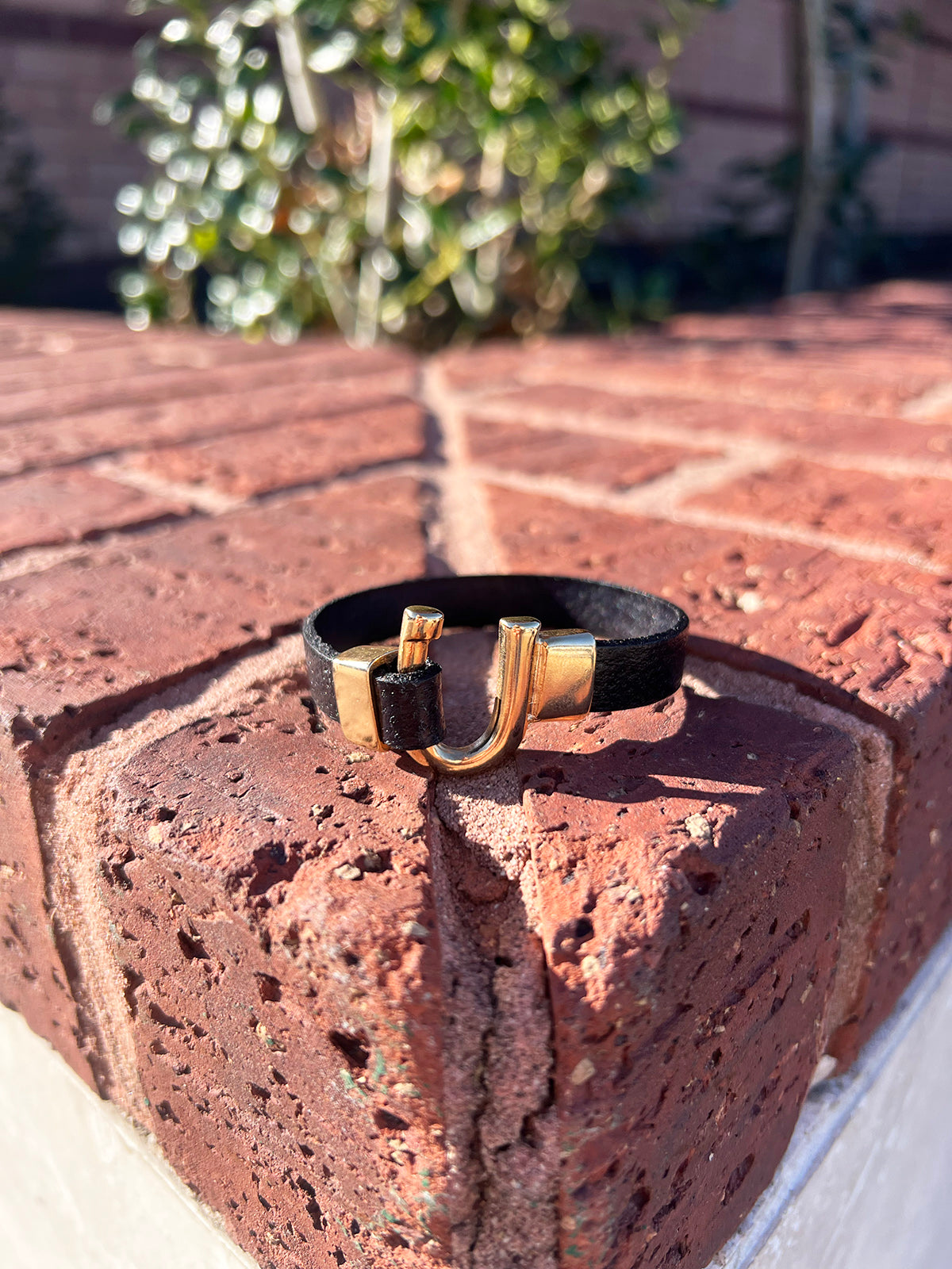 Black and gold bracelet on a brick surface with blurred greenery in the background