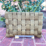 Woven clutch bag on a brick surface with blurred greenery in the background