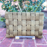 Woven clutch bag on a brick surface with blurred greenery in the background