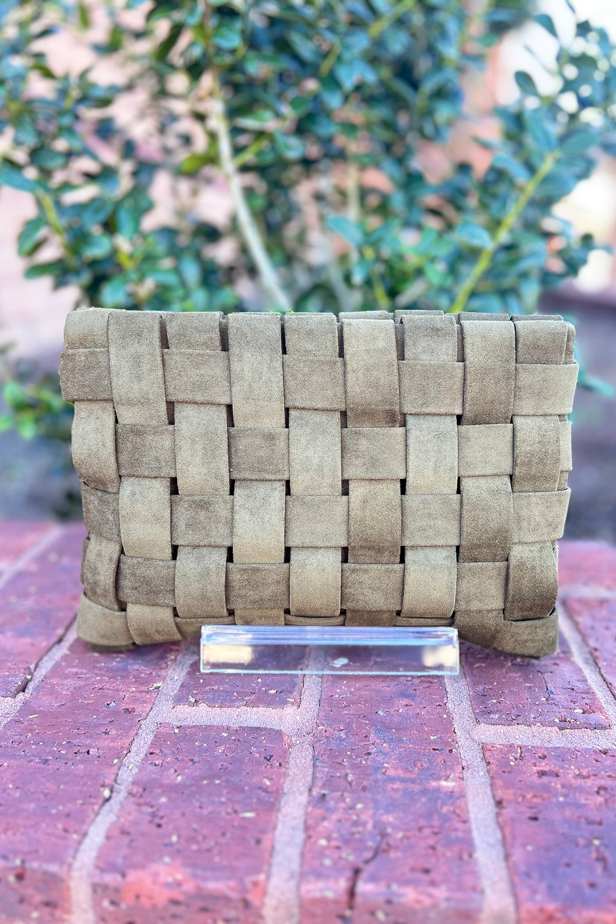 Woven clutch bag on a brick surface with blurred greenery in the background