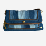 A blue denim crossbody bag with a striped pattern of light and dark blue denim panels, brown leather trim, and gold-tone hardware, shown against a plain white background.