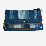 A blue denim crossbody bag with a striped pattern of light and dark blue denim panels, brown leather trim, and gold-tone hardware, shown against a plain white background.