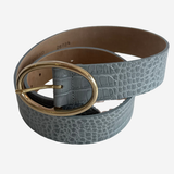 A light blue-gray crocodile-embossed leather belt with a large oval gold-tone buckle, coiled on a light gray background.