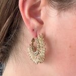 A close-up of a person's ear wearing a gold hoop earring adorned with multiple rows of small white pearls and gold beads.