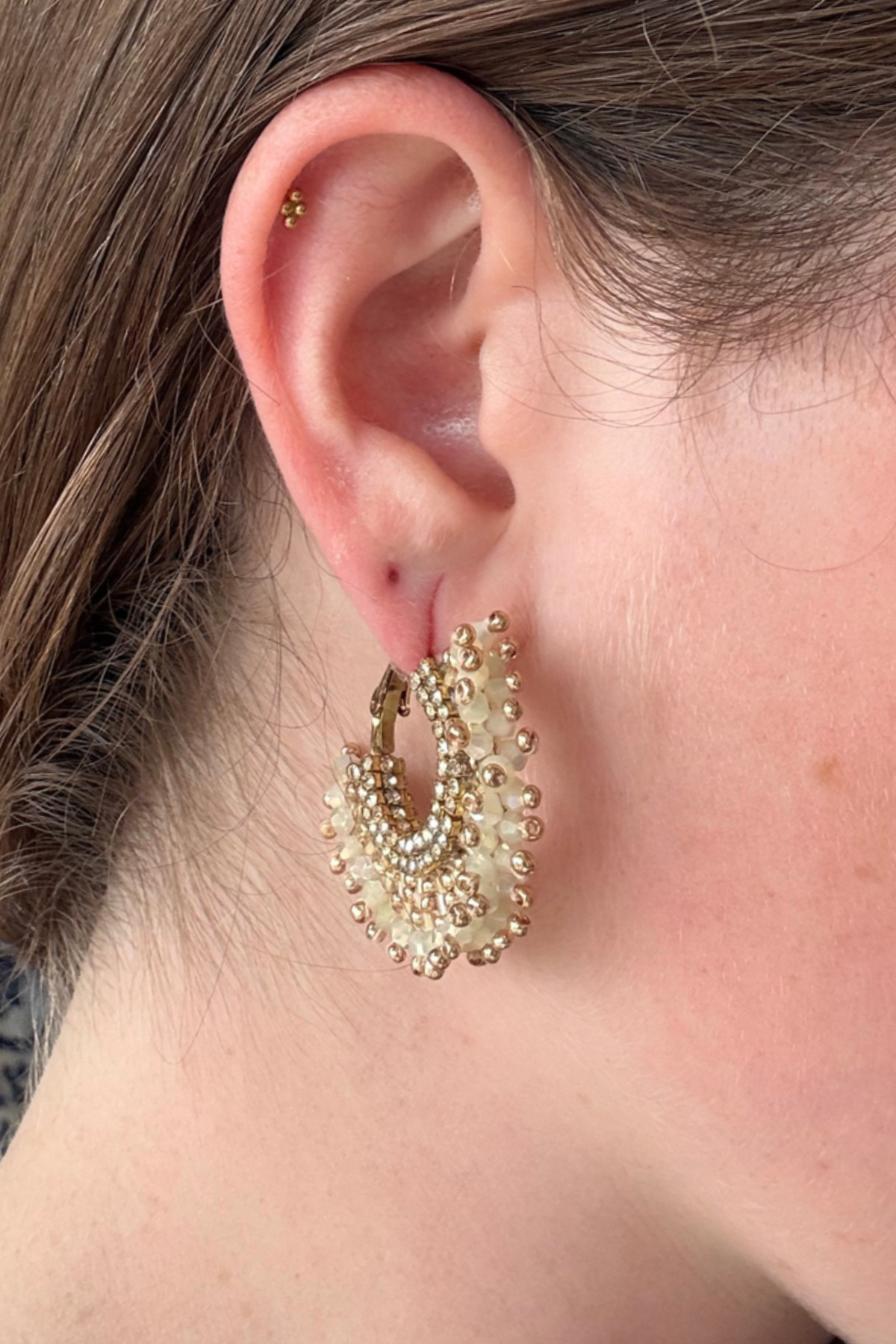 A close-up of a person's ear wearing a gold hoop earring adorned with multiple rows of small white pearls and gold beads.