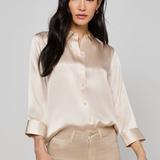Woman wearing a beige satin shirt and pants on a plain background