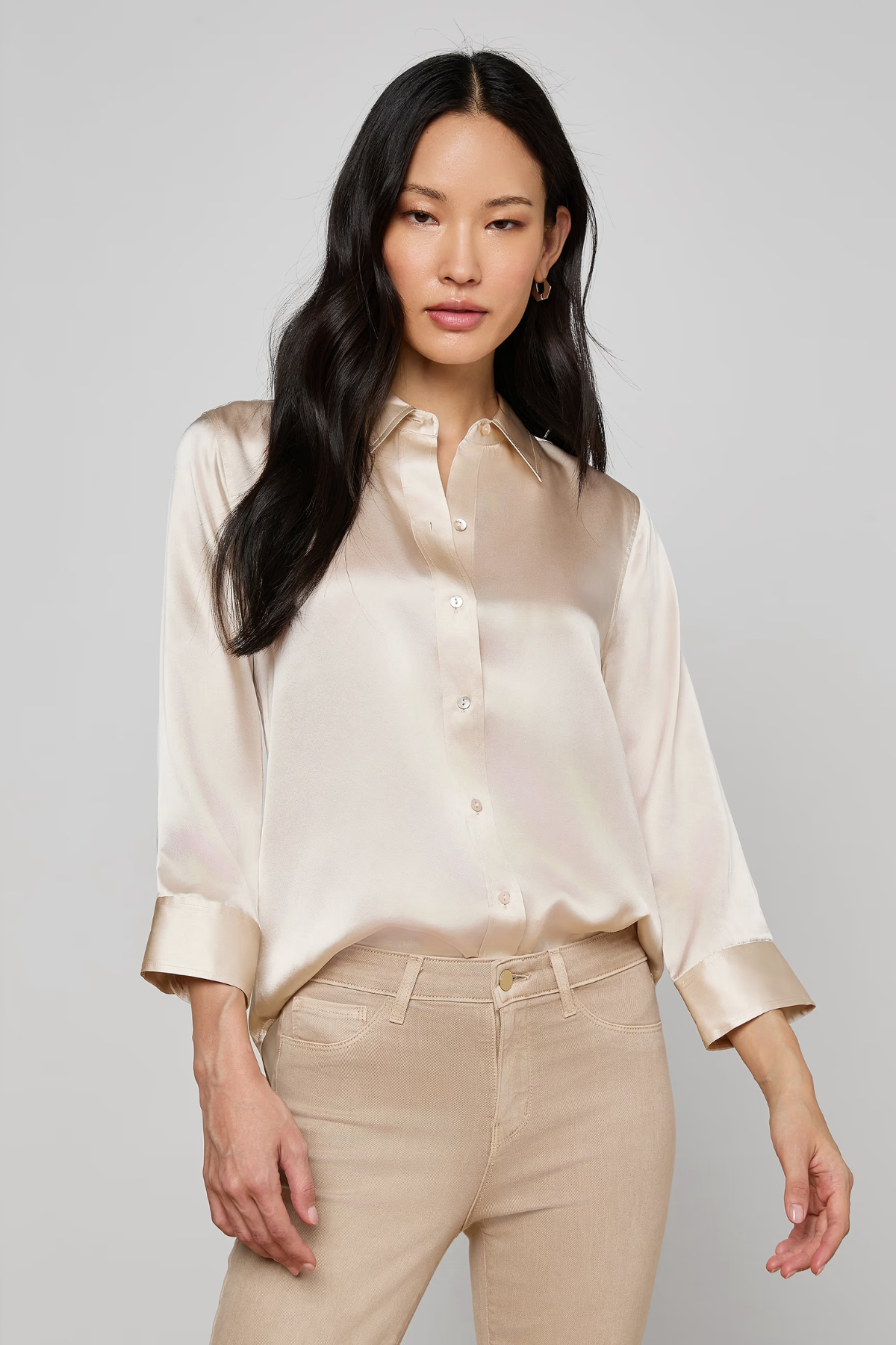 Woman wearing a beige satin shirt and pants on a plain background