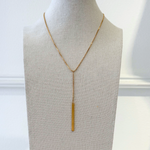Gold lariat necklace on display with white background.