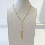 Gold lariat necklace on display with white background.