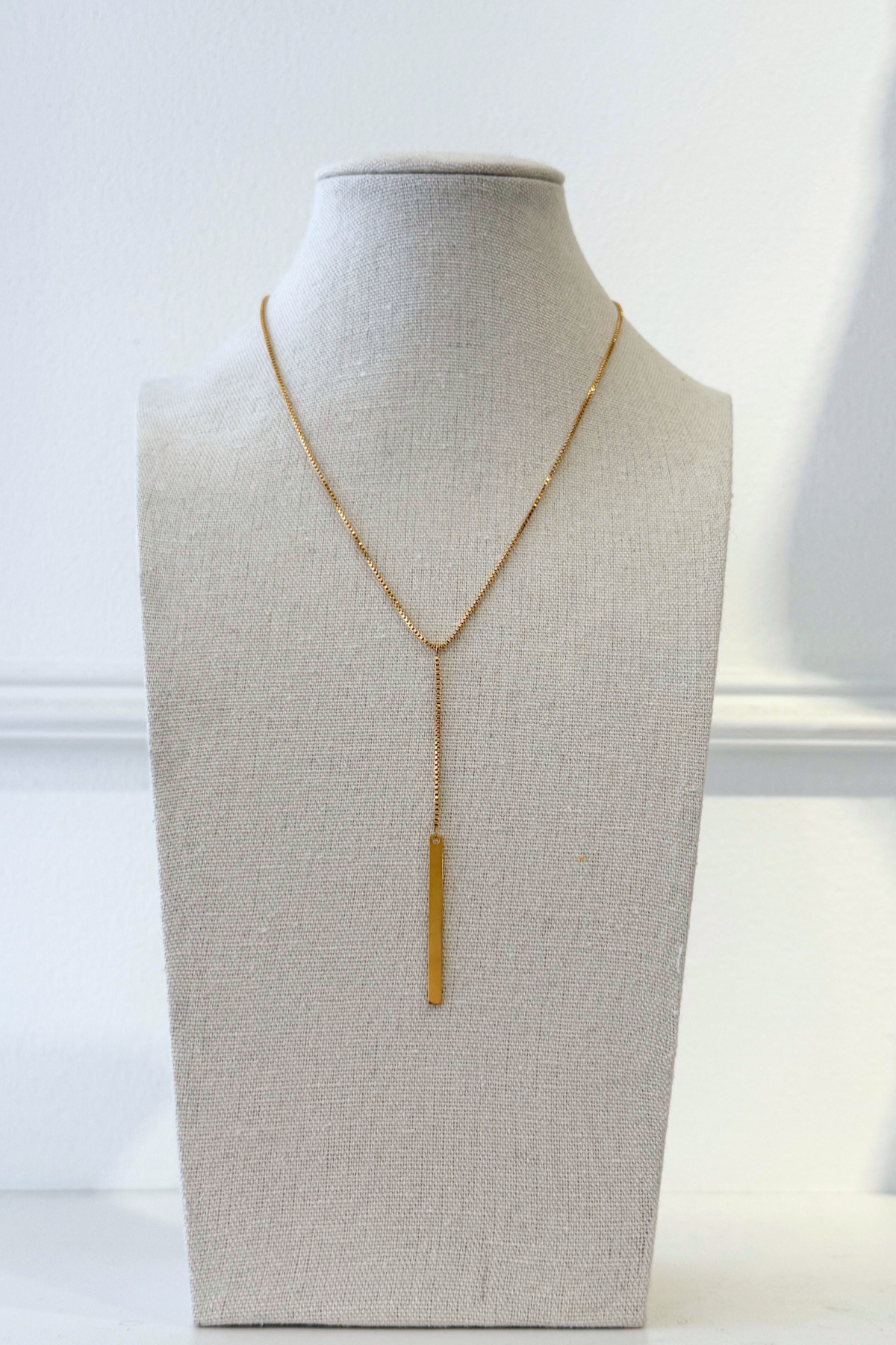 Gold lariat necklace on display with white background.