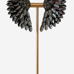 A pair of wing-shaped black rhinestone earrings displayed on a gold T-stand against a light gray background.