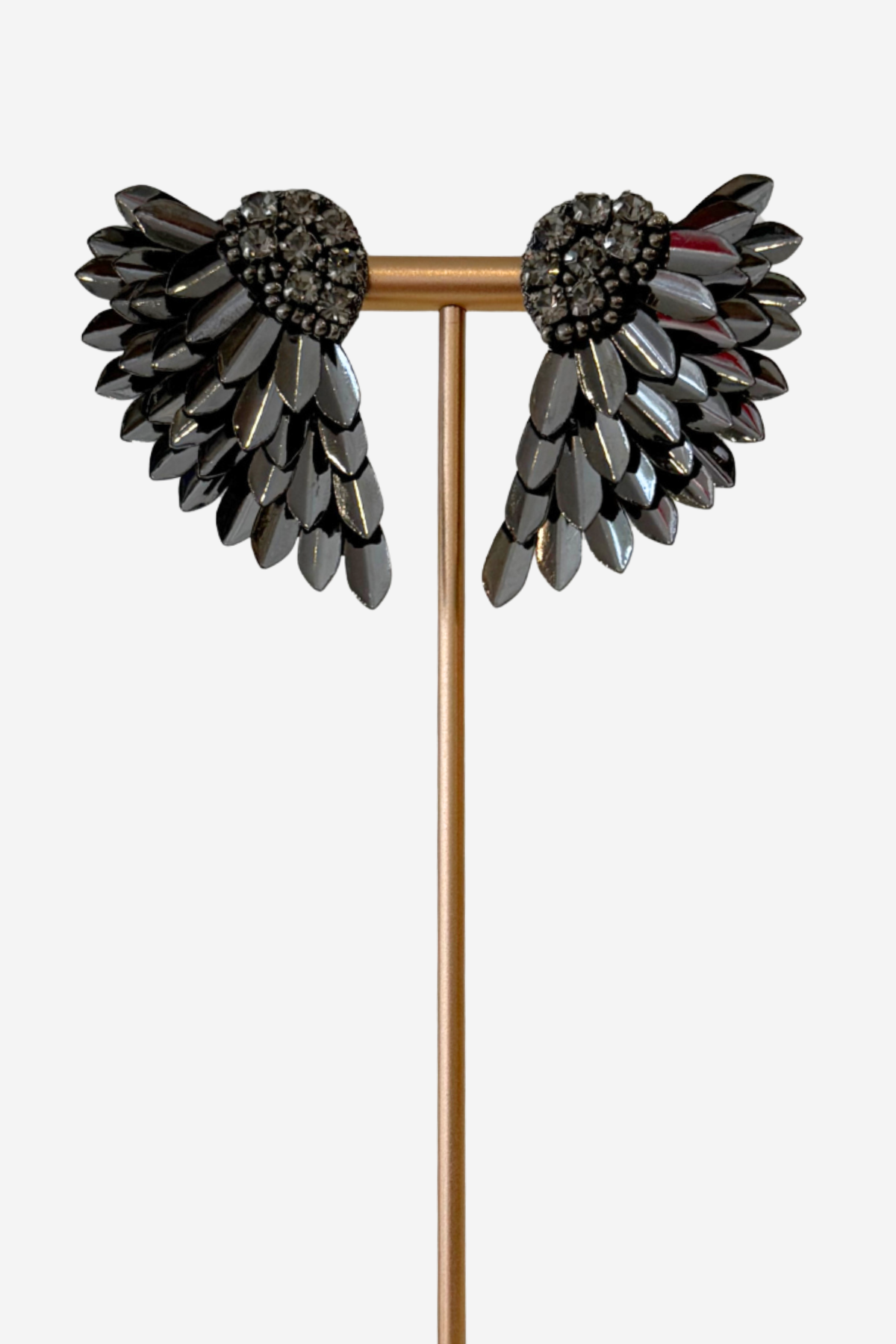 A pair of wing-shaped black rhinestone earrings displayed on a gold T-stand against a light gray background.