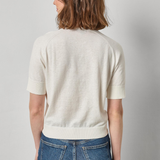 Person wearing a white sweater and blue jeans against a plain background