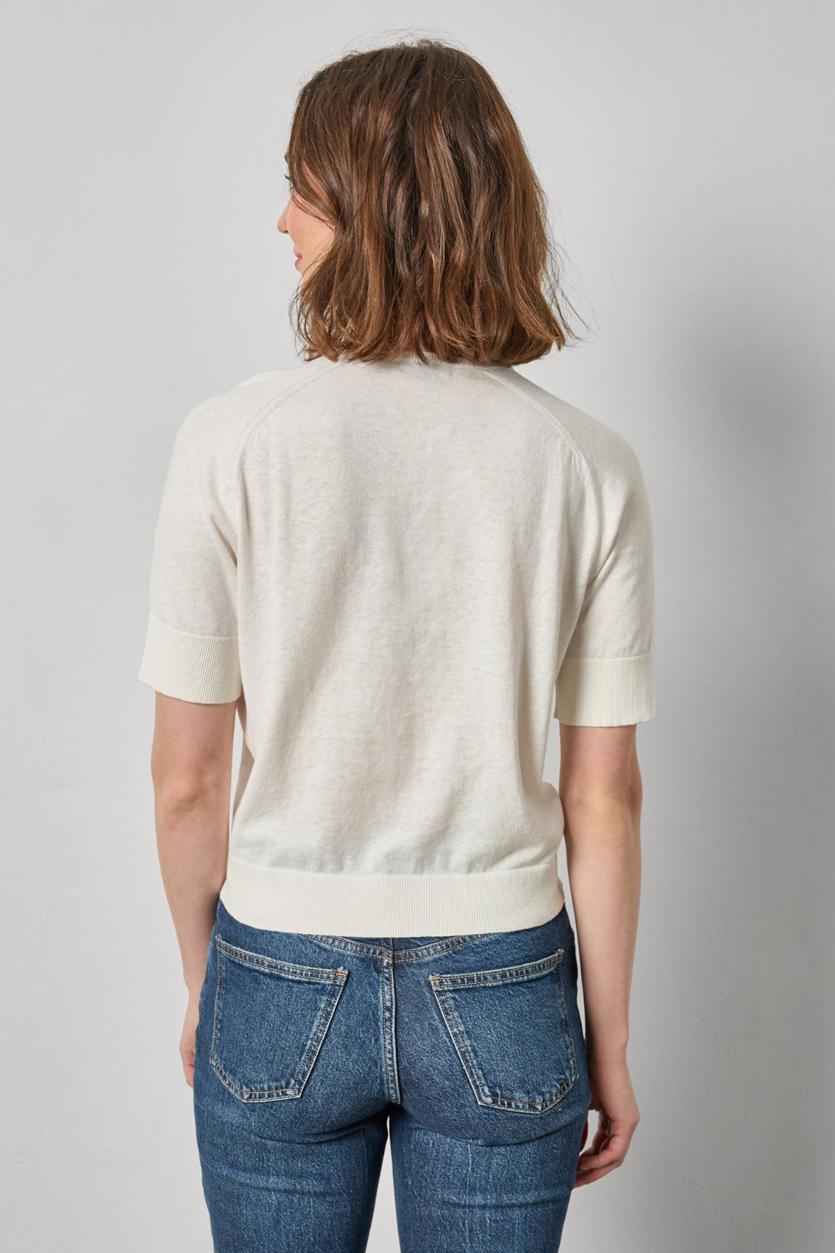 Person wearing a white sweater and blue jeans against a plain background