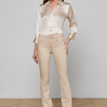 Woman wearing a beige blouse and pants against a white wall.