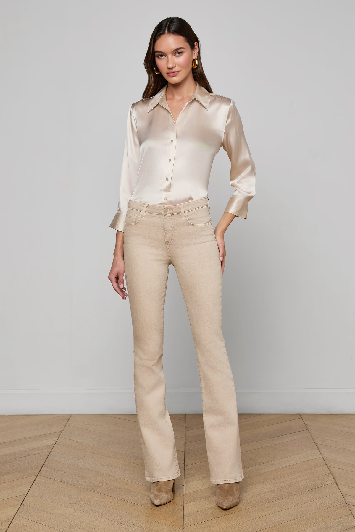 Woman wearing a beige blouse and pants against a white wall.