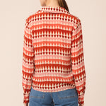 Woman wearing a red and pink patterned shirt with blue jeans on a beige background