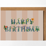 A square birthday card with a kraft envelope, featuring the words 'HAPPY BIRTHDAY' in blue letters decorated with small flowers and green leaves, set against a beige and pink striped background.