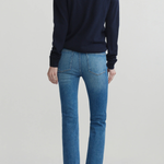 A model shown from the back wearing a dark navy long-sleeve crewneck sweater, blue cropped jeans, and black flats, set against a plain light gray studio background.