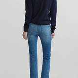 A model shown from the back wearing a dark navy long-sleeve crewneck sweater, blue cropped jeans, and black flats, set against a plain light gray studio background.