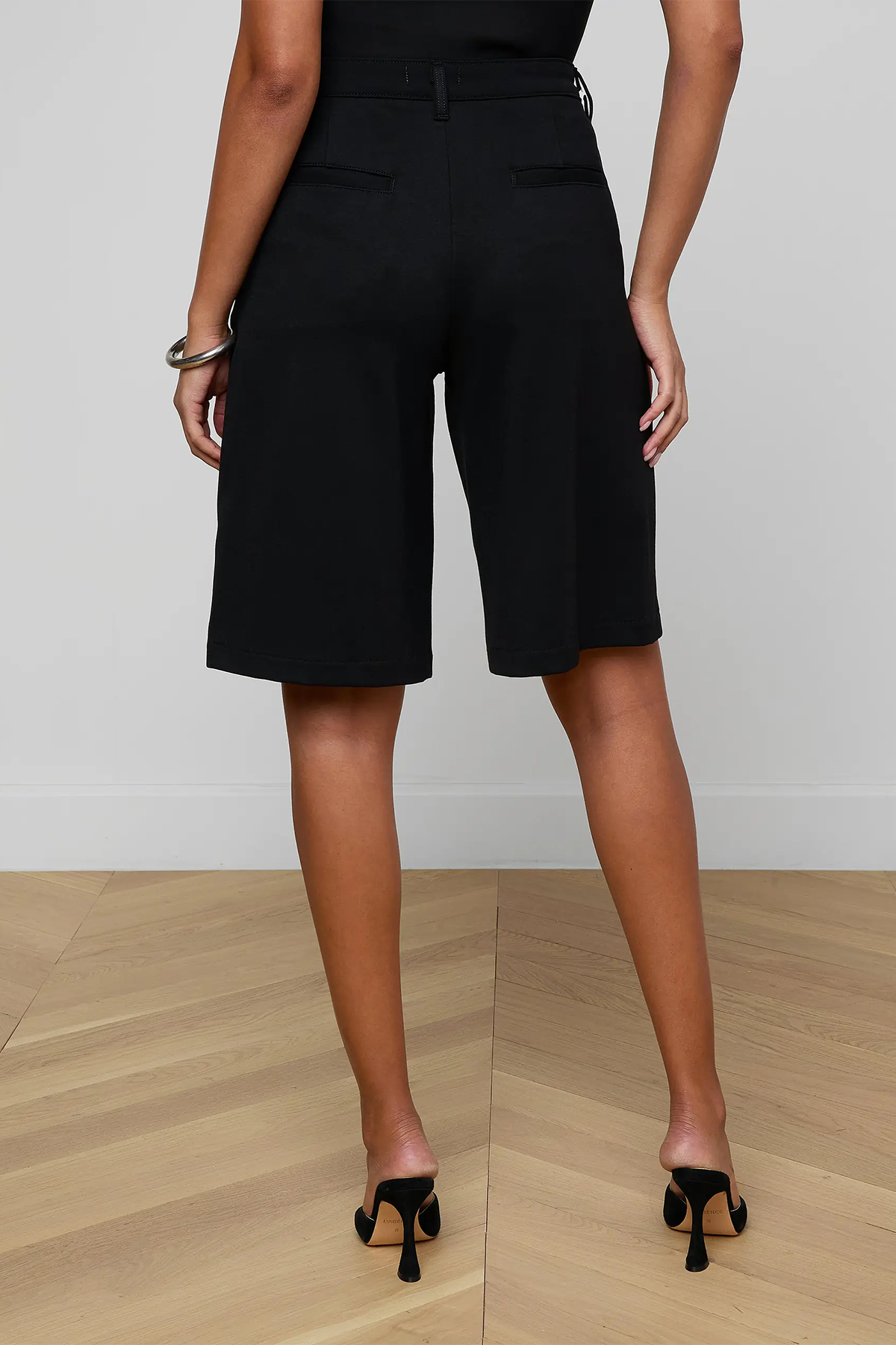 Person wearing black shorts on a wooden floor with a white wall background